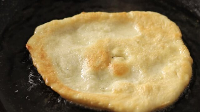 Turkish pisi (deep-fried dough) is cooking in oil in frying pan on the stove. Close-up, selective focus.