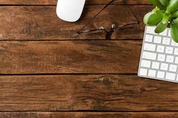 Modern computer keyboard with mouse, eyeglasses and small flower on wooden background. Office...