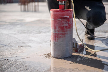 A worker drills a reinforced concrete floor using a drilling rig with a diamond bit.