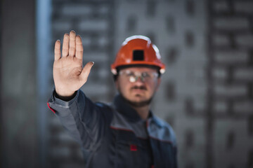 A worker in overalls and a hard hat shows an open palm demonstrating a refusal to work, a crisis in the workplace, a workers' strike.