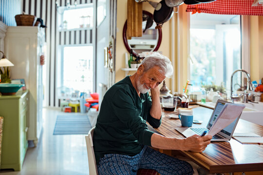 Stressed senior man reading bank statement at home