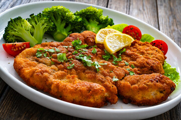 Crispy breaded fried chicken cutlet with boiled broccoli and fresh vegetables on wooden table
