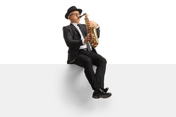 Mature male artist playing a saxophone seated on a blank banner