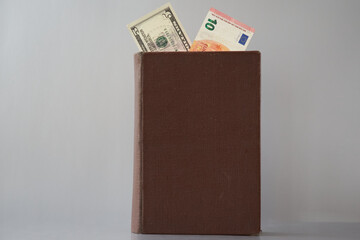 An old book with an untitled cover, showing 10 euros and five dollars, is placed on a gray background. The theme pertains to the laws of international economics and trade, the currency market