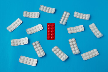 A blister of red tablets among scattered white tablets in blister packs on a blue background. Counterfeit drugs, needed medication, selection of necessary medications