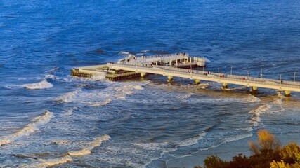 Obraz premium A bird's eye view of the Kołobrzeg pier. Photo taken by a drone showing the pier and the rough, blue Baltic Sea.