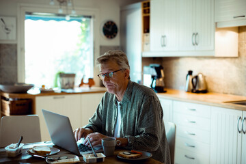 Middle aged man using laptop on kitchen table