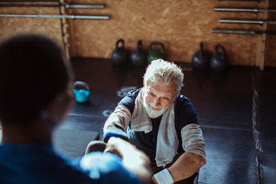 Smiling senior man working out with assistance of personal trainer at gym