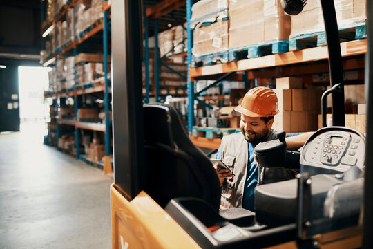 Young male forklift operator using smartphone on break in warehouse