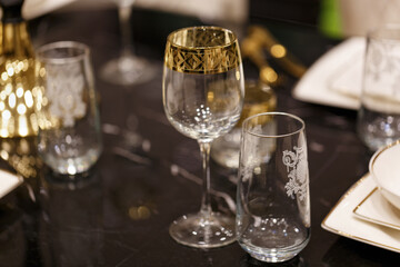 Christmas holiday festive party table with clean glass goblets for wine and gold shiny decoration Christmas, New Year on blurred background. Beautiful two empty glasses standing on a preserved table.