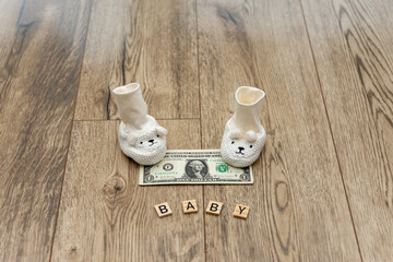 Tiny baby socks on a table with dollar-denominated bills spread out. The concept of the impending birth of a child and care for the state in the form of social.