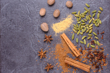 Flat lay of spices on a dark background. Top to bottom Nutmeg, White pepper, Cardamom, Cloves, Star Anise, Cinnamon.