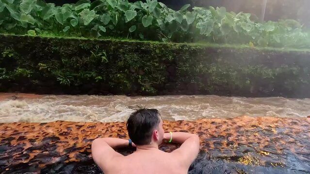 Taking a bath in the thermal water of 'Po&ccedil;a da Dona Beija' in Furnas, Azores, Portugal, with brown hot water next to the river in a rainy day