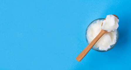 Coconut oil in the wooden spoon and glass jar on the blue background. Top view. Copy space.