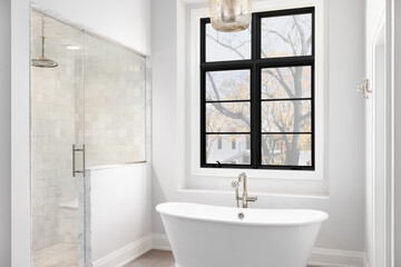 A bathroom detail with light hanging above a freestanding soaker tub, a black large framed window,...