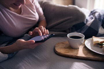 Fototapeta na wymiar Woman having breakfast in bed using smartphone