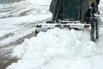 Minitractor bucket clears snow from the neighborhood after a snowstorm. Fragment.