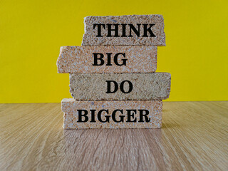 Success achievement concept written on a brick block. Beautiful wooden table, yellow background. Business and Think Big, Do Bigger concept. Motivation quote.