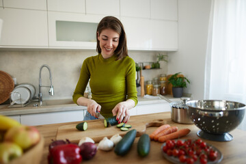 Woman chopping cucumber on the wooden board in the kitchen
