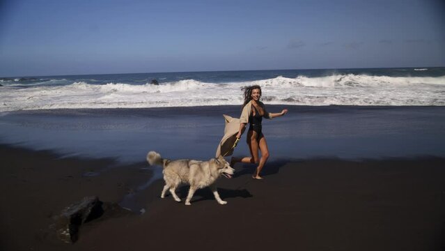 Young beautiful female model running on the beach with her husky dog. Black sand, 4K