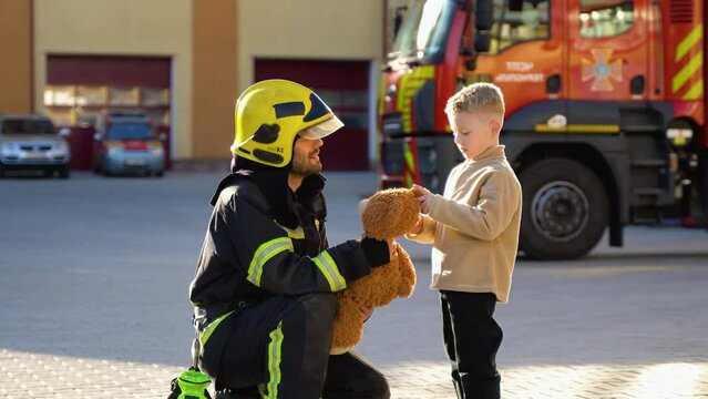 Portrait of rescued little boy with firefighter man standing near fire truck. Firefighter in fire fighting operation