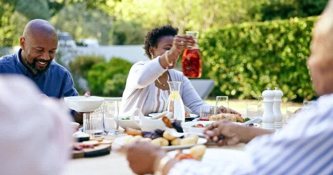 Family, lunch and talking in garden, drink and food to relax in conversation at thanksgiving holiday. Black woman, African man and giving juice with salad, meat or care at event, party or brunch