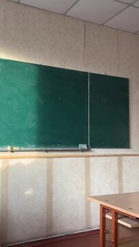 in the classroom there is a green board, the desks are visible, the light of the sun on the board. Empty Classroom with Flying Particles and Sun Rays Entering from Window at Public School