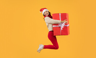 woman leaping holding large wrapped Xmas gift on yellow backdrop