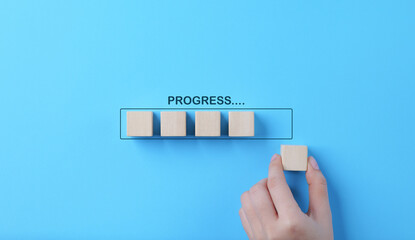 Hand places wooden cubes arranged in row on blue background. with the word progress. in progress,...