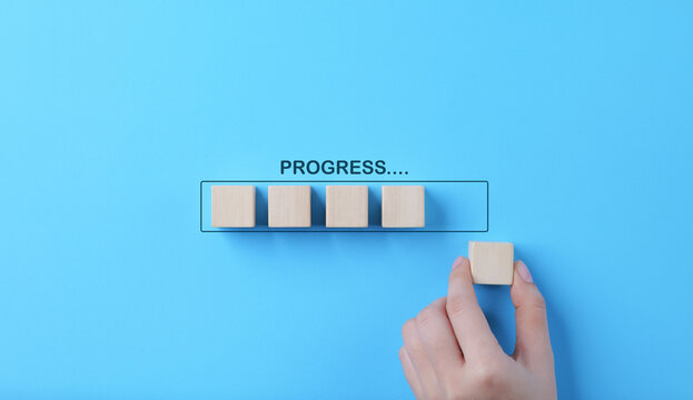 Hand places wooden cubes arranged in row on blue background. with the word progress. in progress, work loading bar, achievement business project plan, Wait for time to success, Work progress concept.