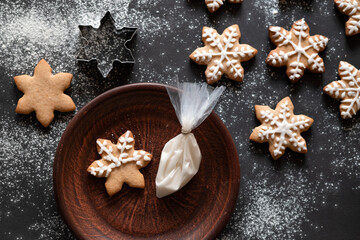 Making traditional Christmas ginger cookie. Star shape gingerbread cookie on black table background with flour and on plate, piping bag with sugar icing. Gingersnap cookie decoration, Selective focus