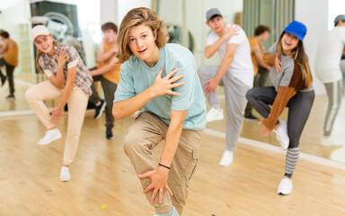 Portrait of expressive teenage krump dancer in choreographic studio with dancing teenagers in...