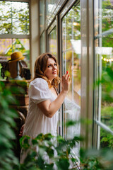 an attractive woman in a white summer dress near a large window in home. 