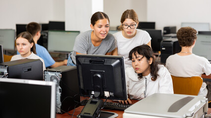 Fototapeta premium Serious teenagers helping to the focused female classmate while she is learning computer science in the class
