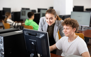 Fototapeta premium Smiling friendly female teacher talking to cheerful teenager studying in college computer lab..