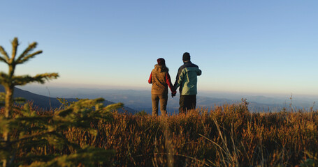 Tourist couple walk beautiful mountain valley. Female traveler with African American man come to admire awesome landscape. Greenery sways by strong wind. Awesome view of nature scenery. Slow motion.