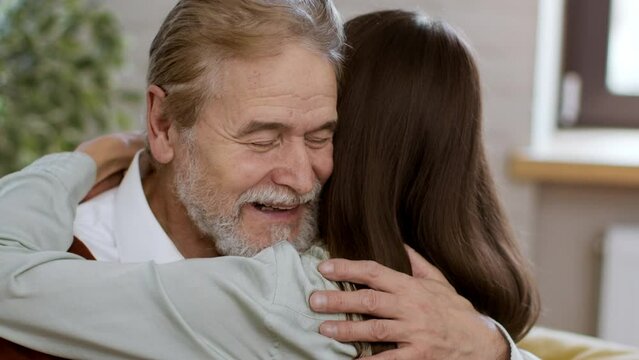 Close up portrait of happy loving senior grandfather embracing his lovely adult granddaughter at home, slow motion