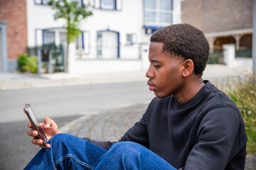 A teenager uses his smartphone sitting on the sidewalk. connected young people