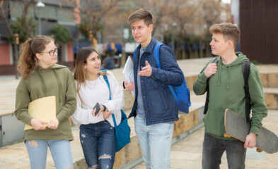 Group of smiling teen pupils chatting after lessons outdoors at warm spring day