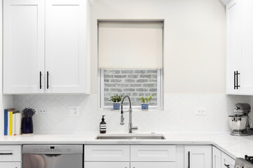 Fototapeta na wymiar A white kitchen detail with an arabesque backsplash tile, a stainless steel faucet and sink, and a white marble countertop.
