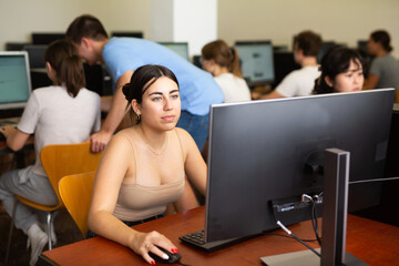 Interested teen girl studying with classmates in school computer class