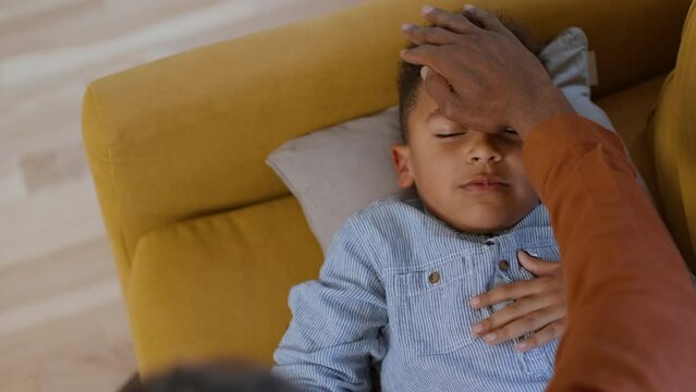 Sickness symptoms. Top view portrait of dreaming little boy on sofa, loving father's hand touching his head, empty space
