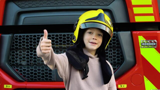 Cute boy, child dressed in fire fighters helmet in a fire station with fire truck. Childs dream