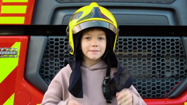 Cute boy, child dressed in fire fighters cloths in a fire station with fire truck. Childs dream