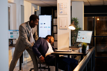 Executive manager wakes up businessman after falling asleep on table desk in startup office. Colleagues working overtime, planning company investment strategy to increase business profit