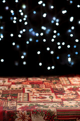 Table with tablecloth, Table with empty Christmas tablecloth with blurred Christmas lights in the background, dark background, selective focus.