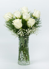 A vertical image of a beautiful bouquets of seven white roses and baby's breath in a glass vase on isolated white background