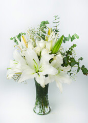 A vertical image of a beautiful all white bouquet of lily, eucaliptus leaves and baby' s breath in a glass vase on isolated on white background