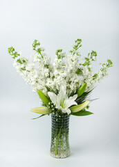 A vertical image of a beautiful bouquet of white delphinium and white lilies in a glass vase on isolated on white background