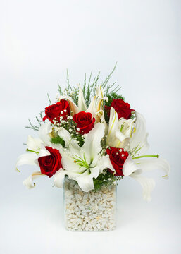 A vertical image of a beautiful bouquet of white lilies and fice red roses in a glass vase on isolated on white background